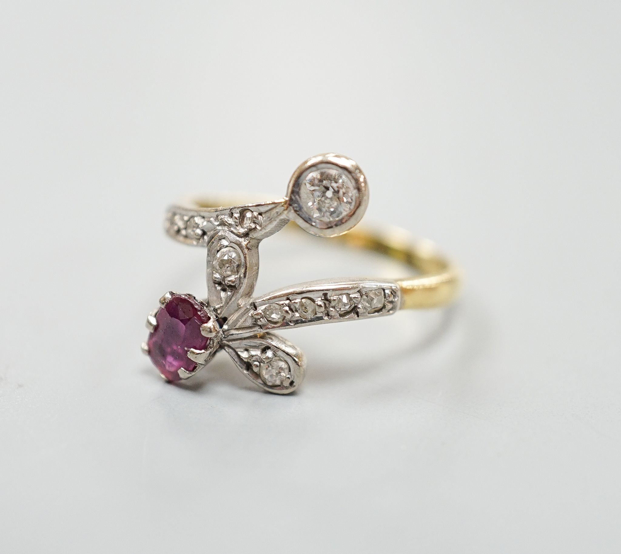 An early to mid 20th century 18ct, ruby and diamond set crossover ring, with diamond set shoulders, size Q/R, gross 4.7 grams.